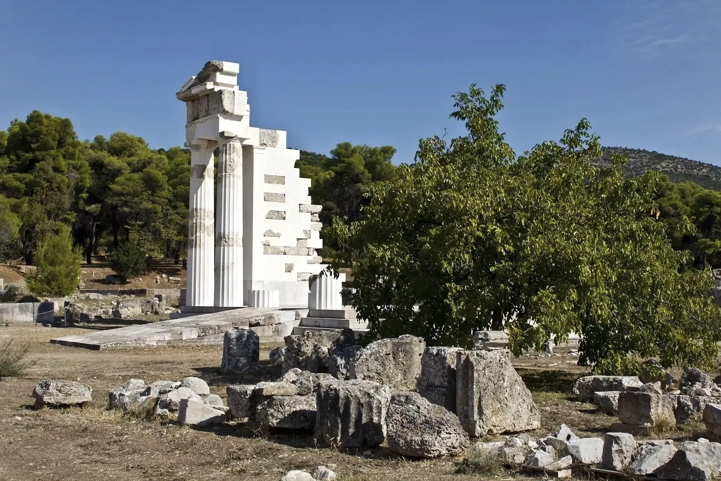 Partly restored Doric columns among ruins and pines at the Sanctuary of Asklepios